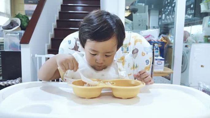 亚洲男婴在高脚椅上吃胡萝卜。