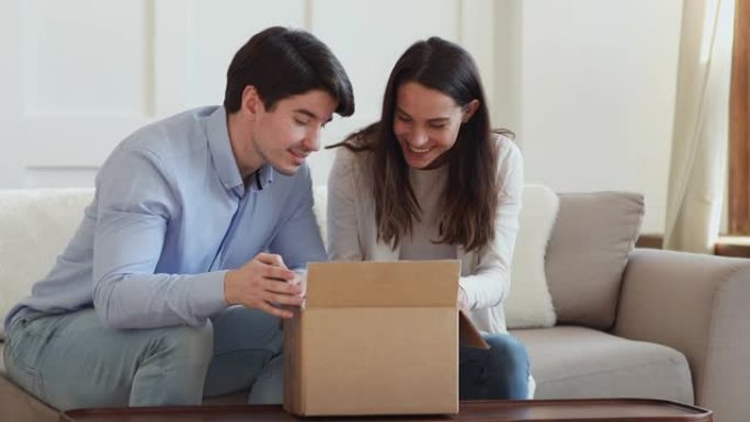 兴奋的年轻夫妇顾客打开纸板箱坐在沙发上