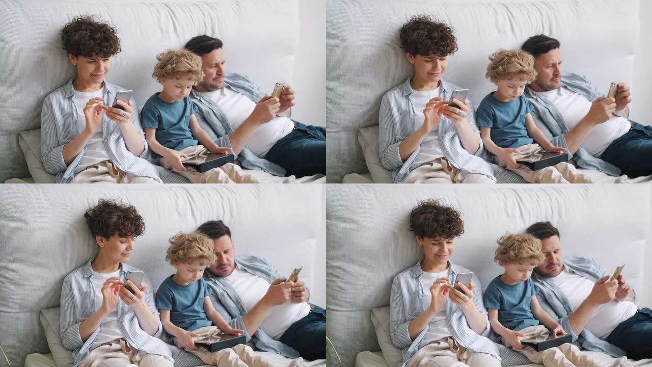 小男孩在平板电脑上玩游戏，而父母在家中床上使用智能手机