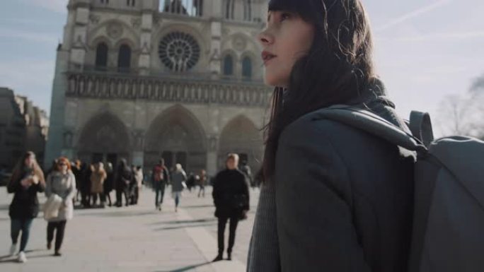 电影向上倾斜，美丽的女人带着背包在阳光明媚的秋日慢动作沿着巴黎圣母院行走。