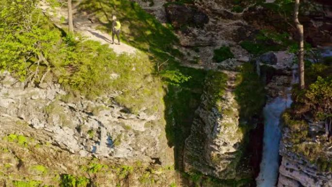 女士女徒步旅行者站在悬崖上的阳光瀑布顶部