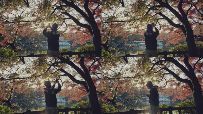 亚洲旅游男子在手机上拍摄湖泊和枫树的照片。