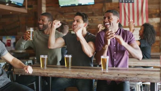 一群男性朋友在体育酒吧的屏幕上观看比赛时庆祝