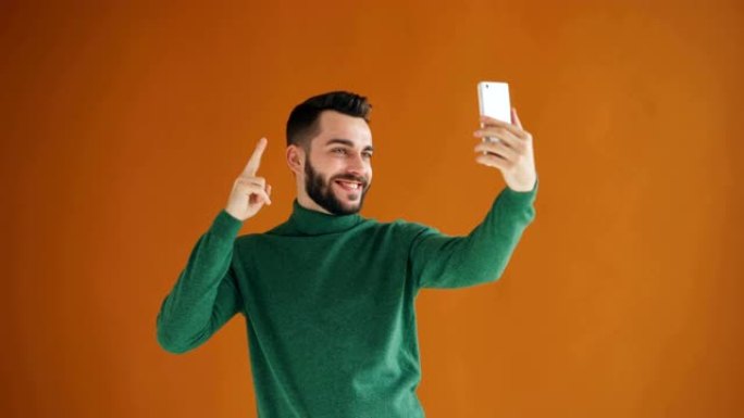 英俊的大胡子男人用智能手机相机自拍的肖像玩得开心