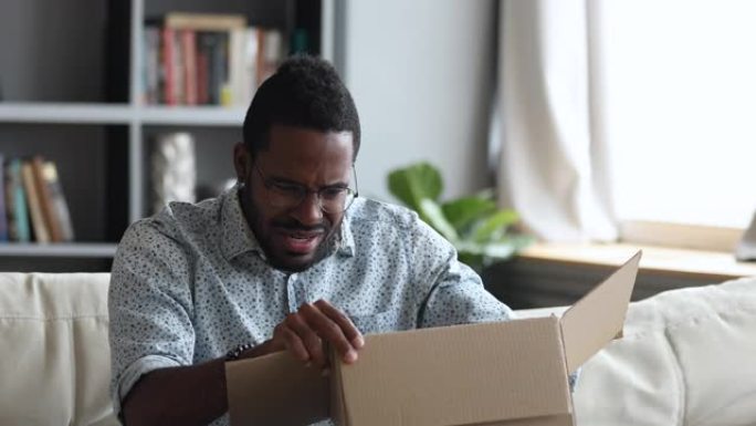 沮丧不满的非洲男子打开纸箱收到不良包裹