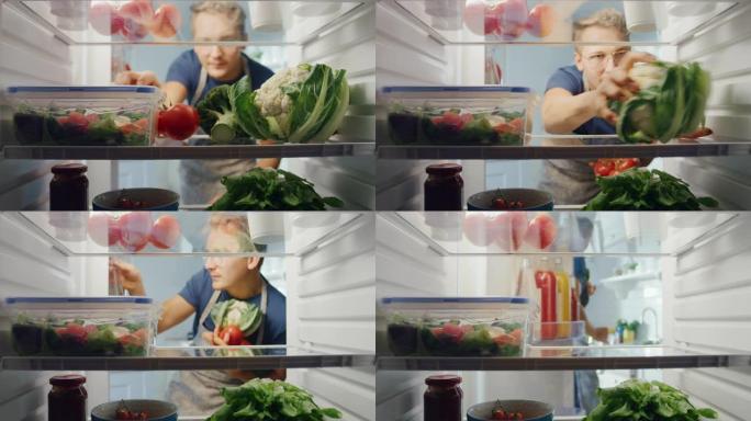 英俊的年轻人打开装满有机食品的冰箱，抓起一堆蔬菜做沙拉。饮食和健康的生活观念。冰箱里的视点。