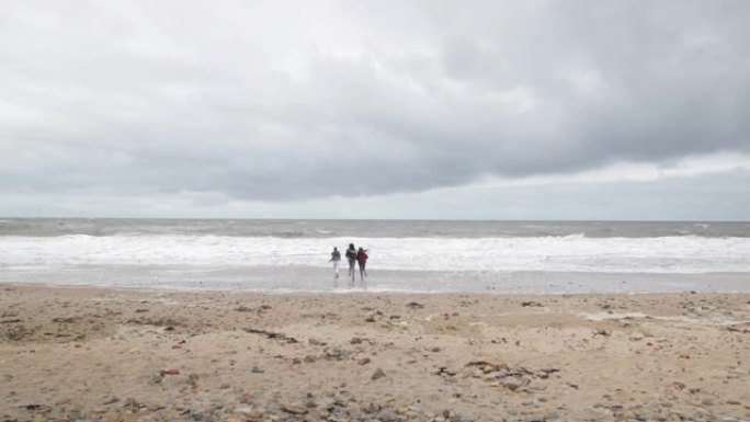 十几岁的女孩在多风的海滩上追逐海浪