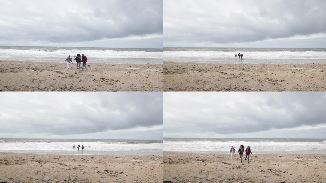 十几岁的女孩在多风的海滩上追逐海浪