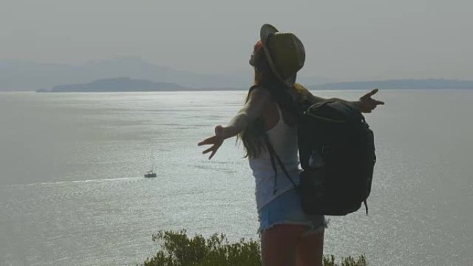 一位旅游摄影师的女人拿着电话，背着背包感到自由，可以欣赏到蔚蓝的海和天空。