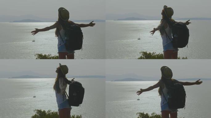 一位旅游摄影师的女人拿着电话，背着背包感到自由，可以欣赏到蔚蓝的海和天空。