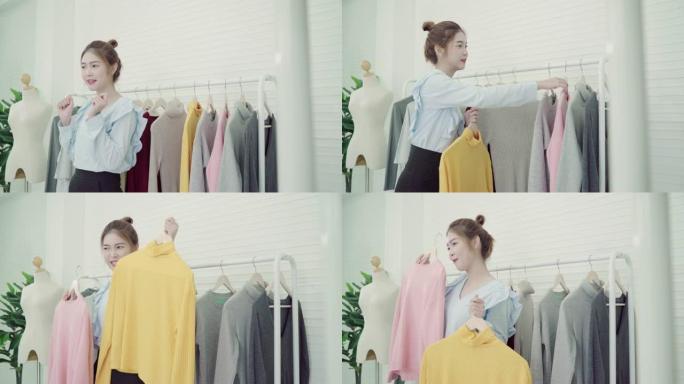 亚洲时尚女博主网红拿着购物袋和挂在衣架上的大量衣服录制新时尚视频，在家通过互联网向社交网络直播。