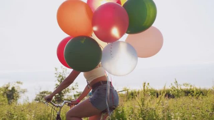 年轻女子骑着自行车，在乡村中装饰着五颜六色的气球，以慢动作射击。