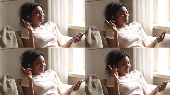 非洲妇女靠在沙发上，使用智能手机耳机听音乐