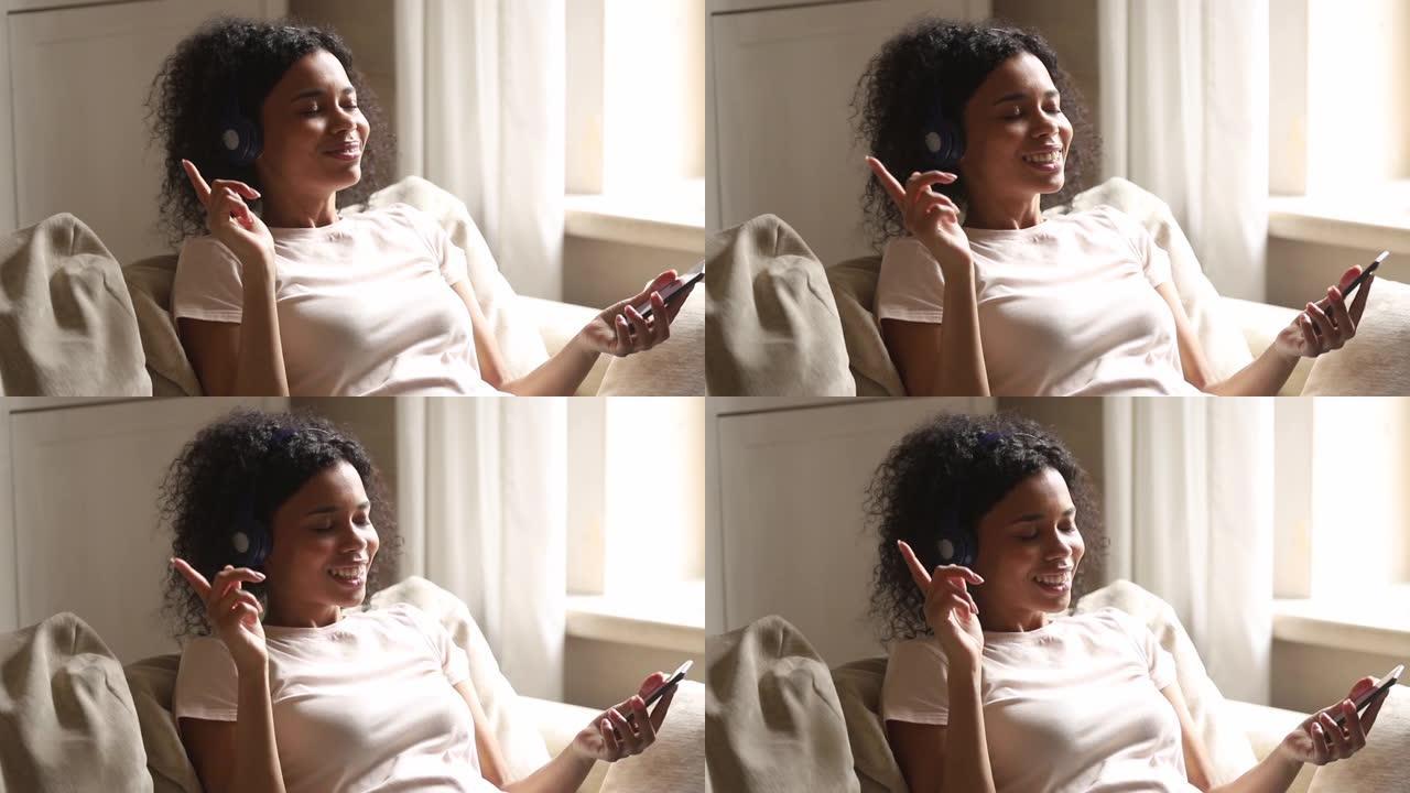 非洲妇女靠在沙发上，使用智能手机耳机听音乐