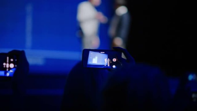 观众使用智能手机在商务会议上录制两名演讲者。在观众席上，公众使用手机拍摄两位明星主持人的视频，现场活