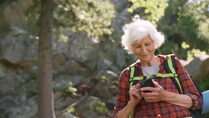 在森林中使用智能手机打字的高级女性