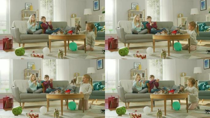 在家: 可爱的女孩在视频游戏机中玩耍，使用操纵杆控制器，她的年轻兄弟为她欢呼，最小的孩子玩玩具恐龙。