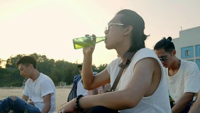 年轻的亚洲成年人坐在沙滩上放松喝啤酒
