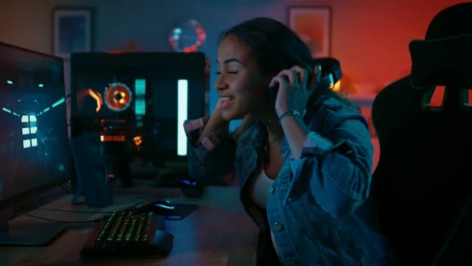 一个漂亮而兴奋的黑人游戏女孩的肖像，戴着耳机在她的电脑上玩第一人称射击游戏在线视频游戏。她转身对着镜