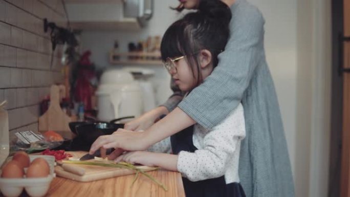 千禧一代的母亲用女儿的帮助手在家做饭煎蛋卷在厨房准备早餐。