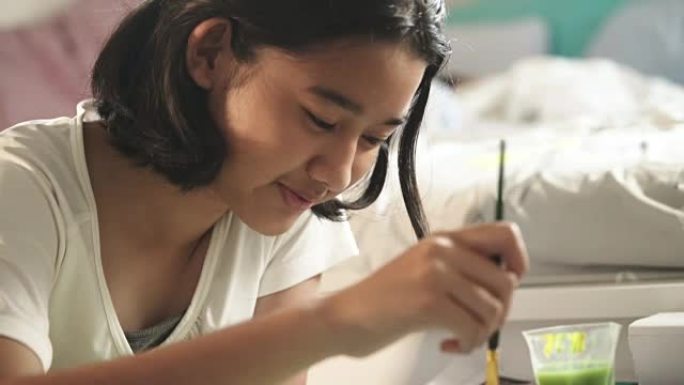 亚洲年轻女孩用画笔和水彩画在她的房间里