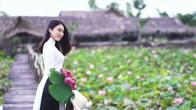 4k慢动作镜头越南美女肖像手持粉红色莲花在大莲花湖木桥上微笑，越南，亚洲或东南亚旅行概念