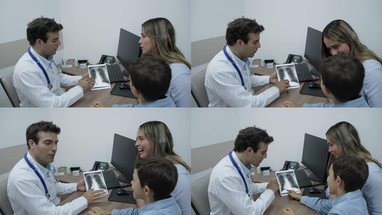 友好的医生在平板电脑上展示了他的儿科患者肺部的x射线，同时与他和妈妈愉快地讨论