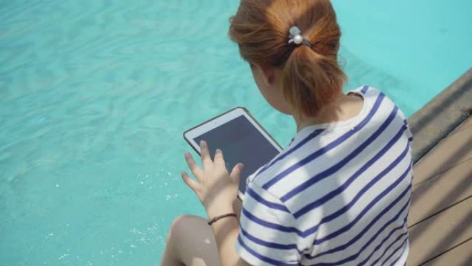 使用数字平板电脑坐在游泳池附近的女性