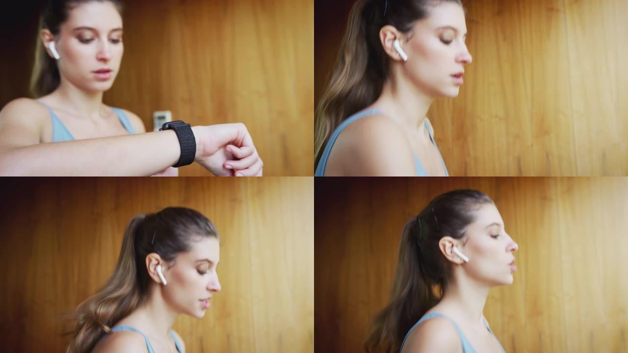 女人在家跑步机上锻炼戴着无线耳机检查智能手表