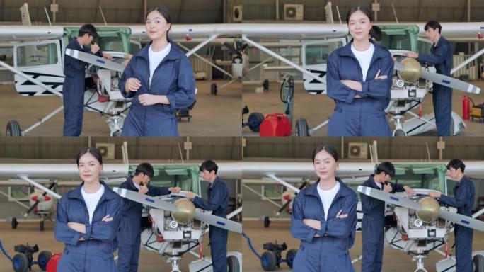 领导亚洲十几岁的女孩站着，双臂交叉微笑着为机库飞机的开发工程师维护而充满信心。STEM中的妇女，工作