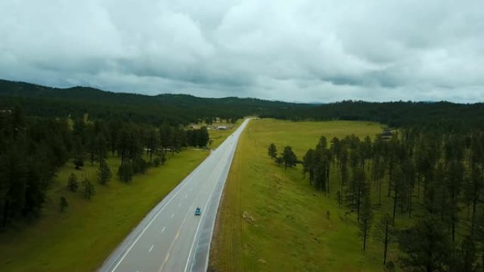 蓝色三轮车在野生绿色森林山丘与树木之间的美国高速公路上快速行驶的惊人航拍