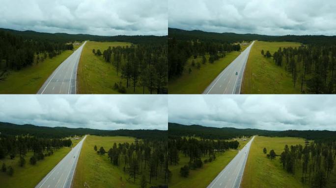 蓝色三轮车在野生绿色森林山丘与树木之间的美国高速公路上快速行驶的惊人航拍