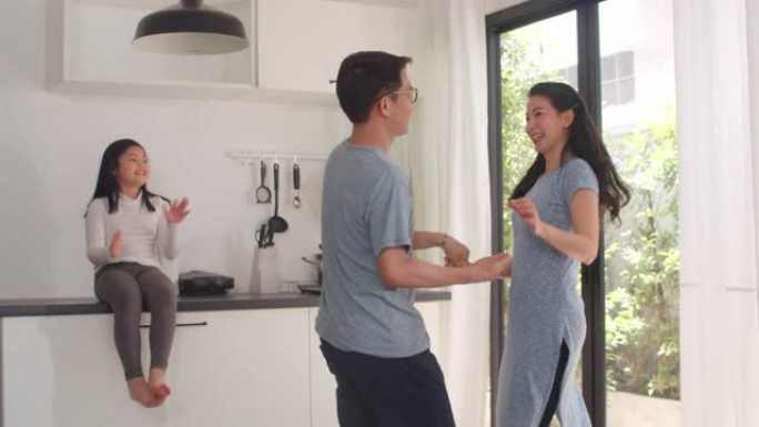 快乐年轻的亚洲家庭在家里吃完早餐后听音乐跳舞。日本母亲父亲和孩子女儿早上在现代厨房里一起度过时光。慢