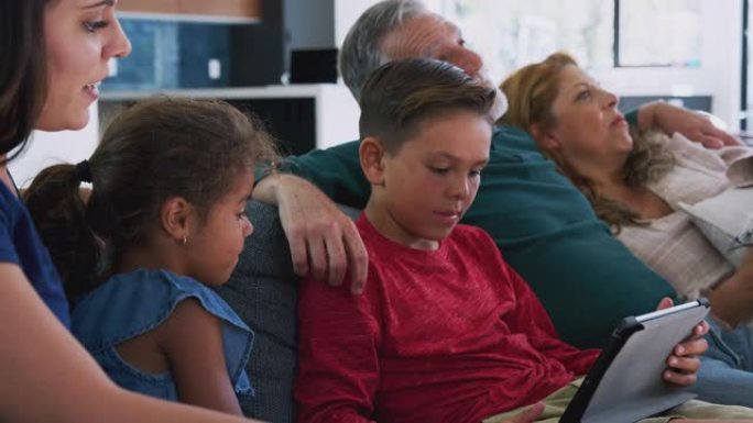 当孙子玩数字平板电脑时，多代西班牙裔家庭在沙发上放松