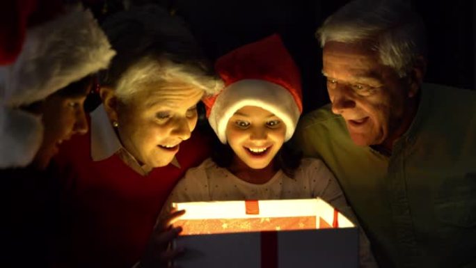 可爱的小女孩晚上打开圣诞礼物，她的祖父母和哥哥都微笑着