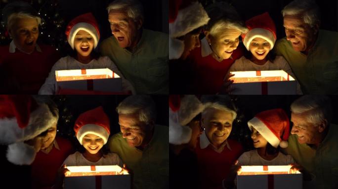 可爱的小女孩晚上打开圣诞礼物，她的祖父母和哥哥都微笑着
