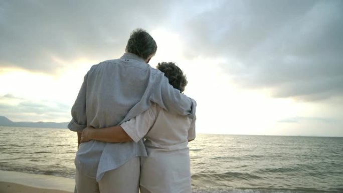 亚洲老年夫妇在海滩上慢动作拥抱。