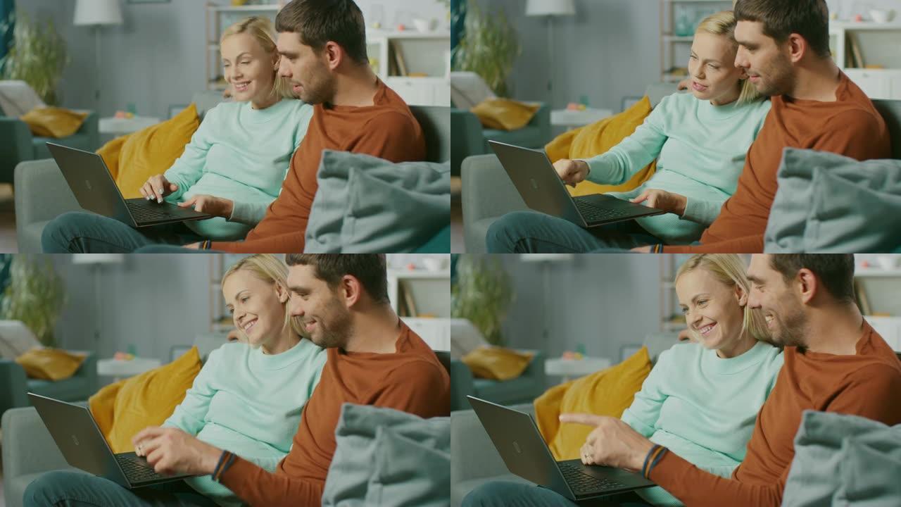 可爱的年轻夫妇坐在家里的沙发上，他们使用笔记本电脑，玩得很开心。美丽幸福的年轻夫妇恋爱的肖像。