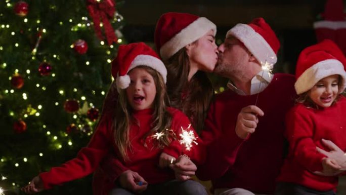 戴着圣诞老人帽子的快乐快乐家庭的慢动作，手里拿着烟火唱着圣诞歌曲。