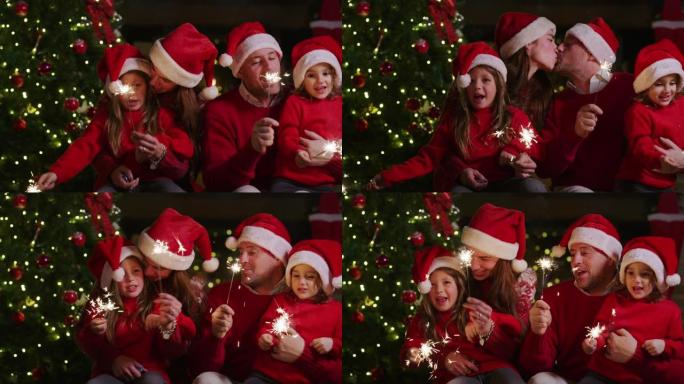 戴着圣诞老人帽子的快乐快乐家庭的慢动作，手里拿着烟火唱着圣诞歌曲。