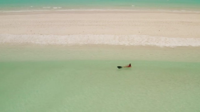 一个女人躺在肚子上漂浮在荒岛上干净的大海中的鸟瞰图。