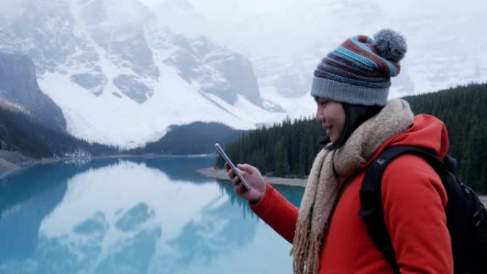 在加拿大冰碛湖使用手机的年轻女性旅行者