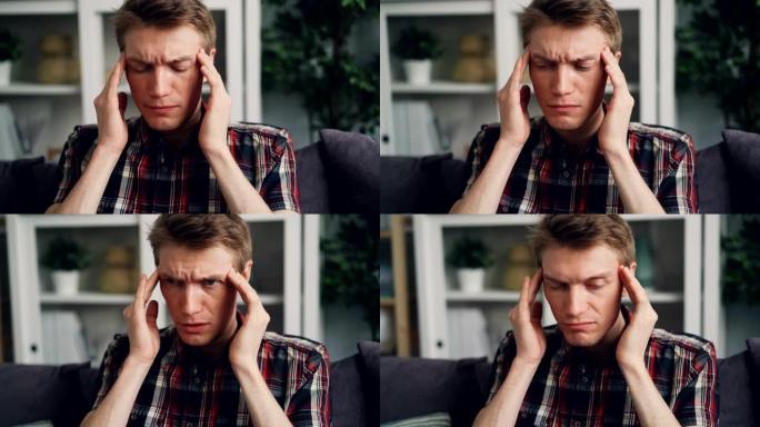 年轻人患有严重的头痛，抚摸着他的头部在家里按摩太阳穴。