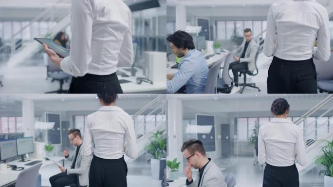 在明亮的公司办公室中: 手持数字平板电脑的女高管走过办公室，她的专业员工在台式计算机上工作。后续镜头