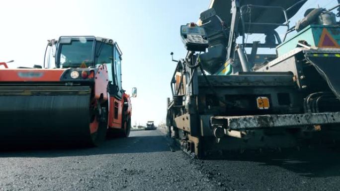 新鲜的沥青路面，铺路机在前视图中。道路施工过程。