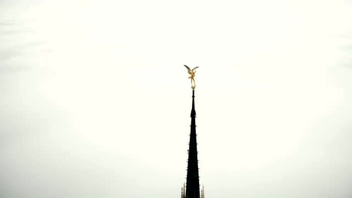 无人机在圣米歇尔要塞山顶上的金色圣迈克尔雕像周围飞行，在云层上方的阳光下发光
