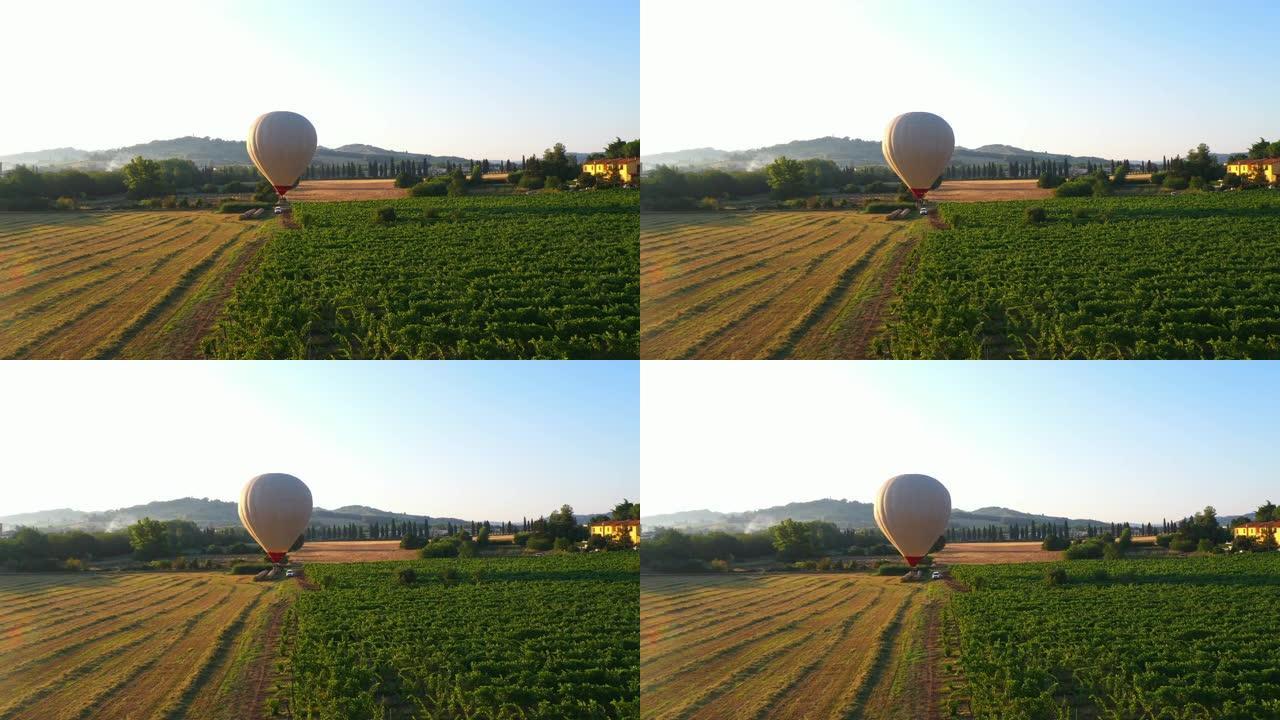 空中无人机镜头: 热气球飞越美丽的田野和种植园，背景是山