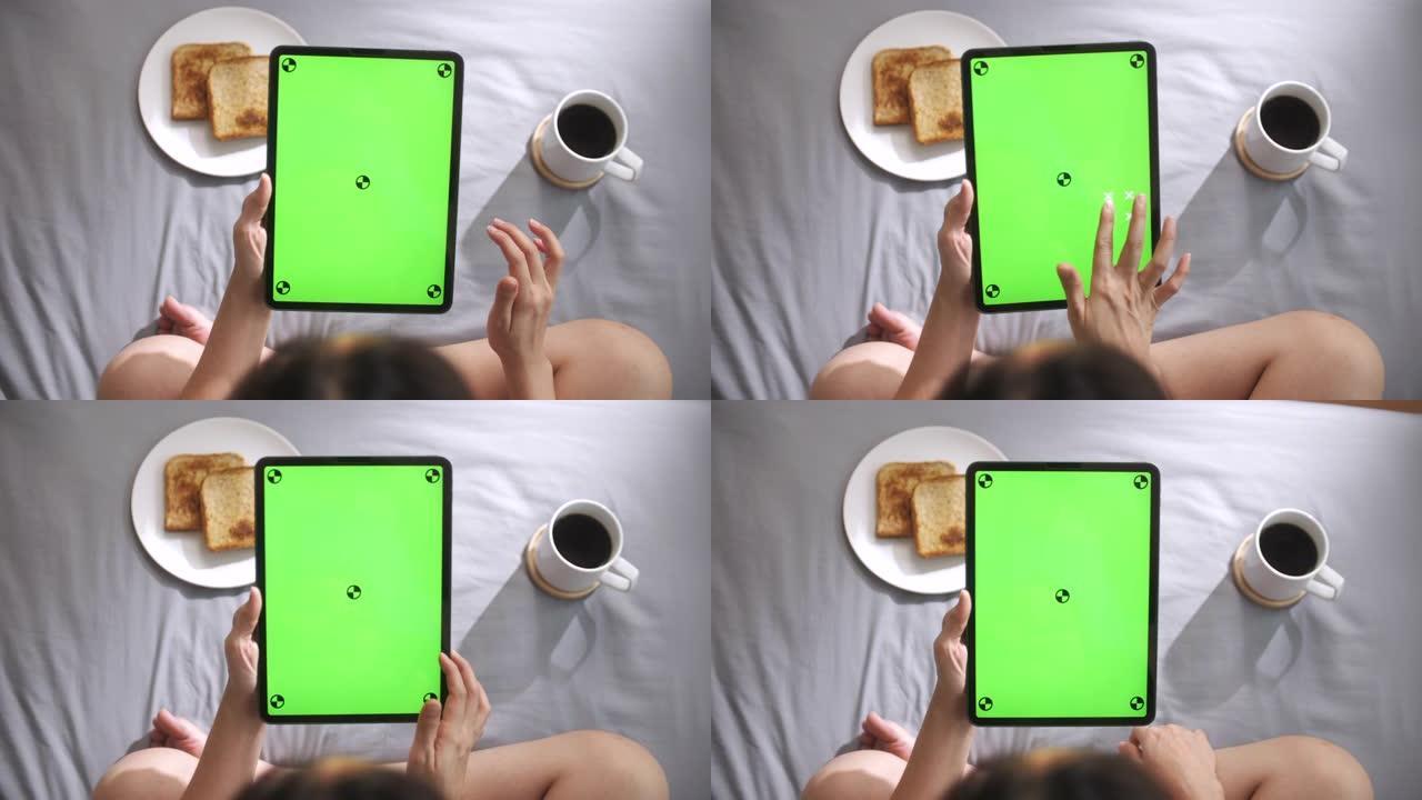 女人使用和看数字平板电脑，早上在床上绿色屏幕，垂直