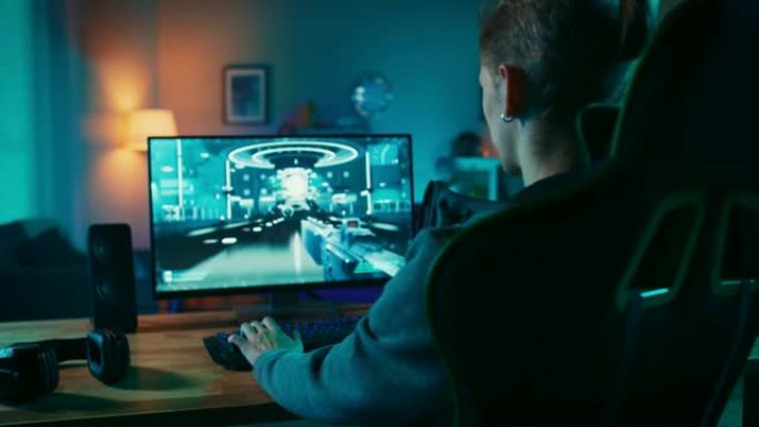 玩家在其功能强大的个人计算机上玩第一人称射击游戏在线视频游戏的背面照片。房间和电脑有彩色霓虹灯。在家