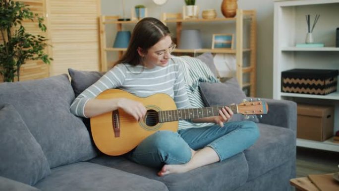 戴眼镜的美女弹吉他坐在家里沙发上摆莲花姿势